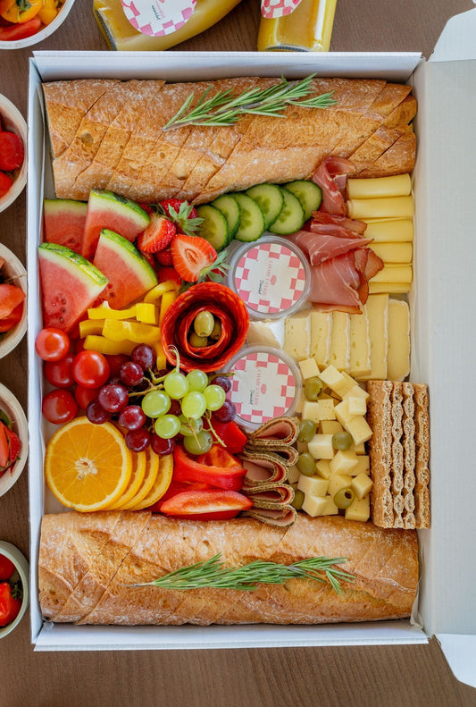Charcuterie Box including baguette, cheese, sausages, fruits, veggies, dips and jam. Decorated beautifully in a catering box. 